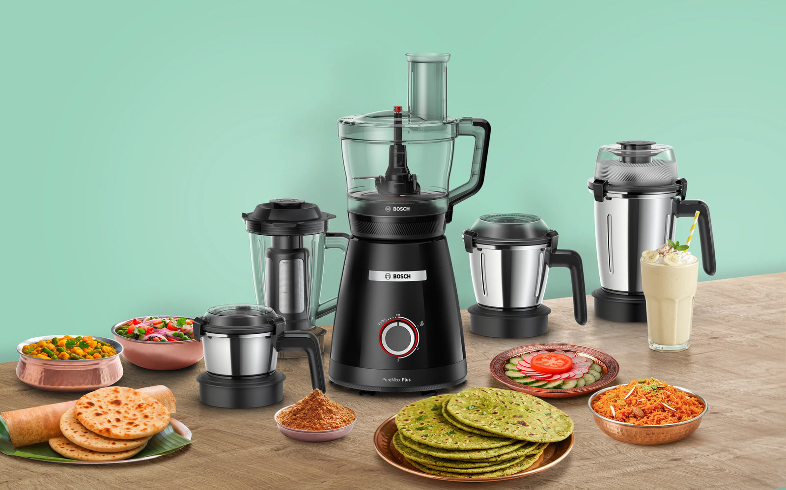 Bosch food processor with various food items on a wooden table against a green background
