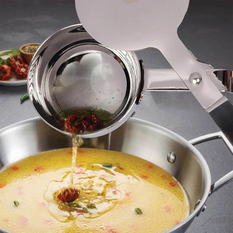 Stainless steel ladle pouring liquid into a pot of soup on a gray surface.