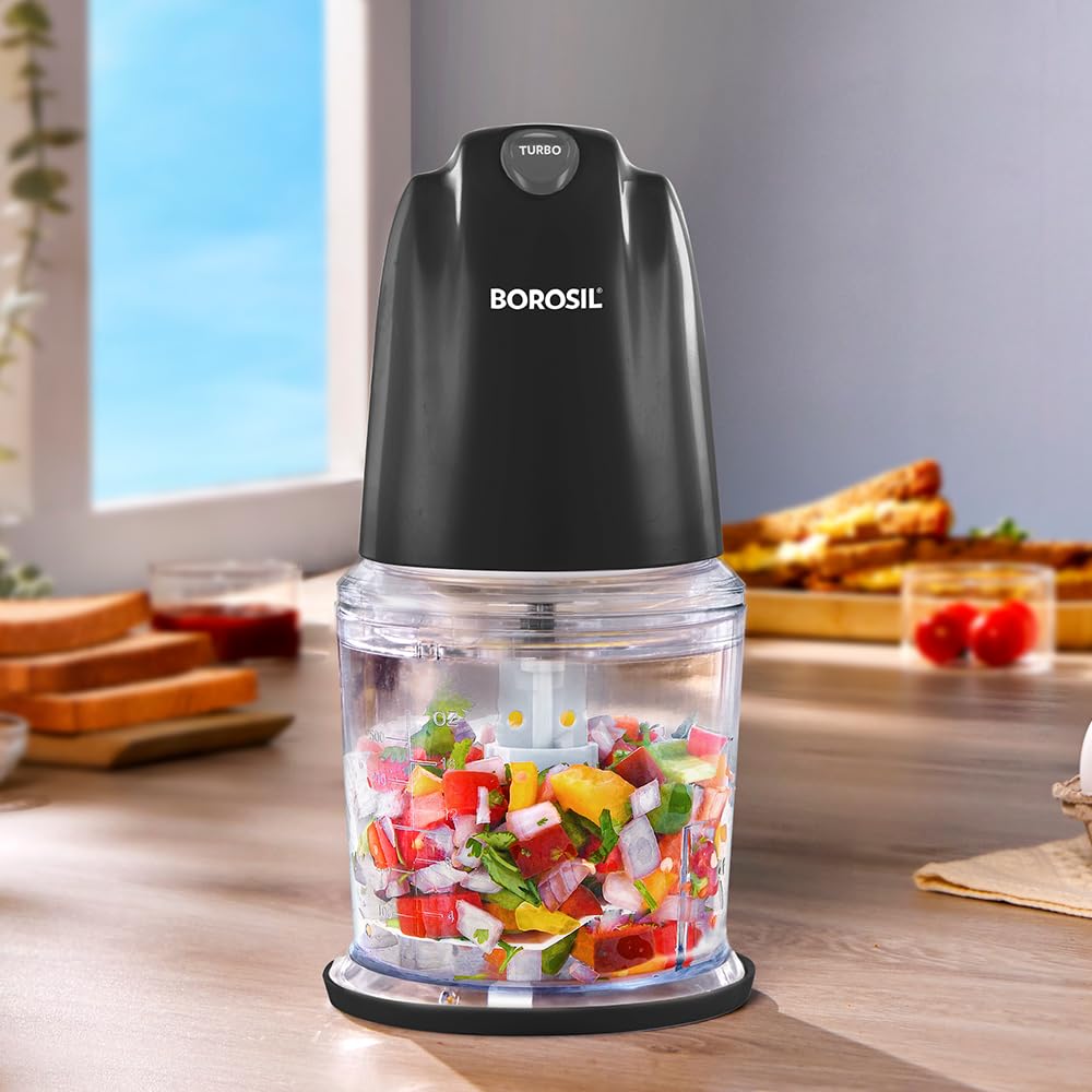 A black BOROSIL electric food chopper with a clear jar filled with chopped vegetables, set on a wooden countertop in a kitchen environment.