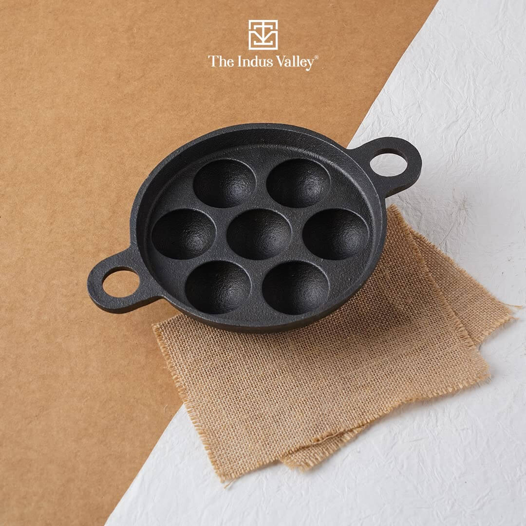 Indus Valley cast iron paniyaram pan with 7 pits on a textured surface, highlighting its pre-seasoned non-stick design.